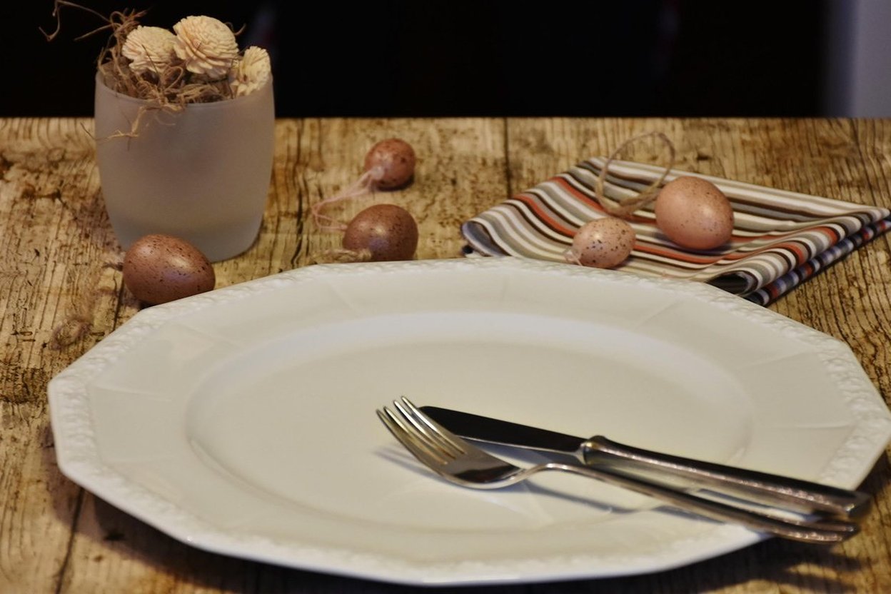 An empty white plate with a knife and fork on a rustic wooden table.