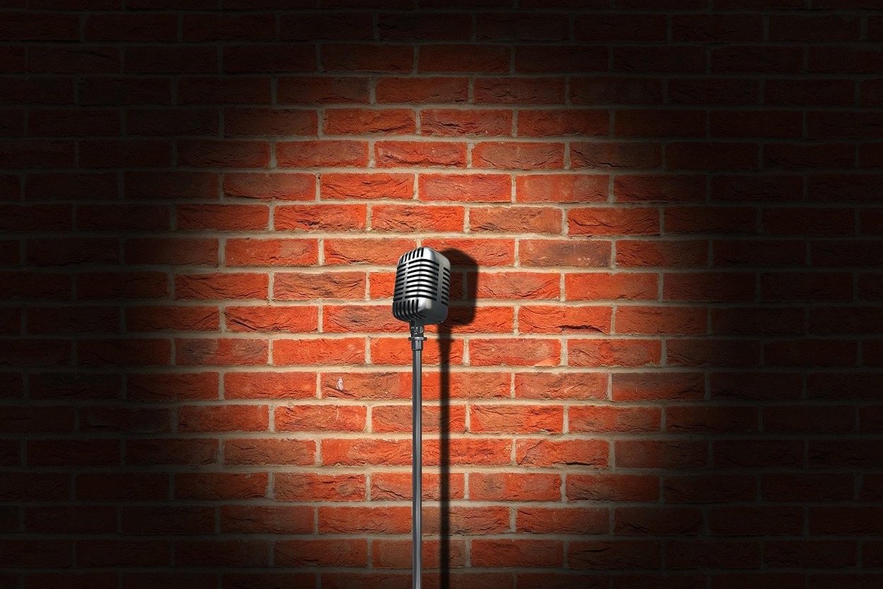 A vintage microphone on a stand in front of a brick wall, like a comedy club stage.