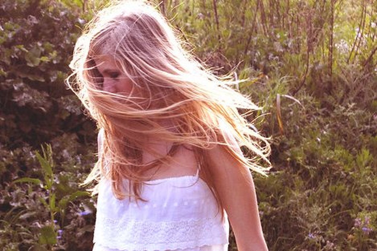 A woman with long natural blonde hair blowing in the wind outdoors.