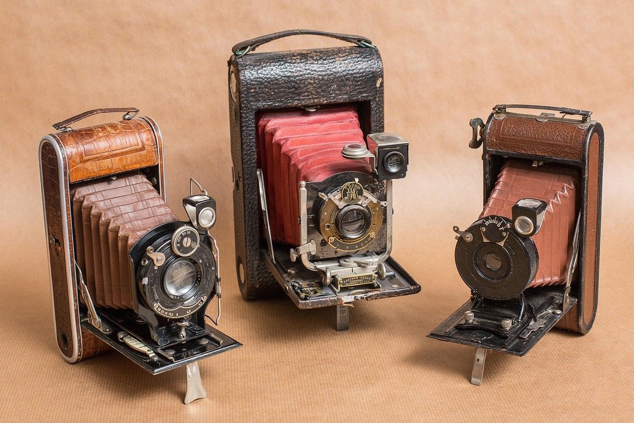 Three vintage folding cameras with leather cases and bellows.