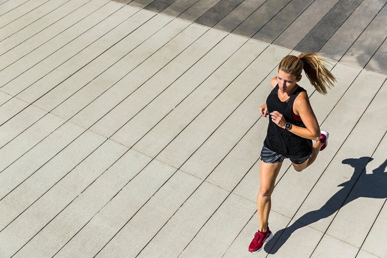 A runner on a sunlit wooden boardwalk, casting a long shadow.