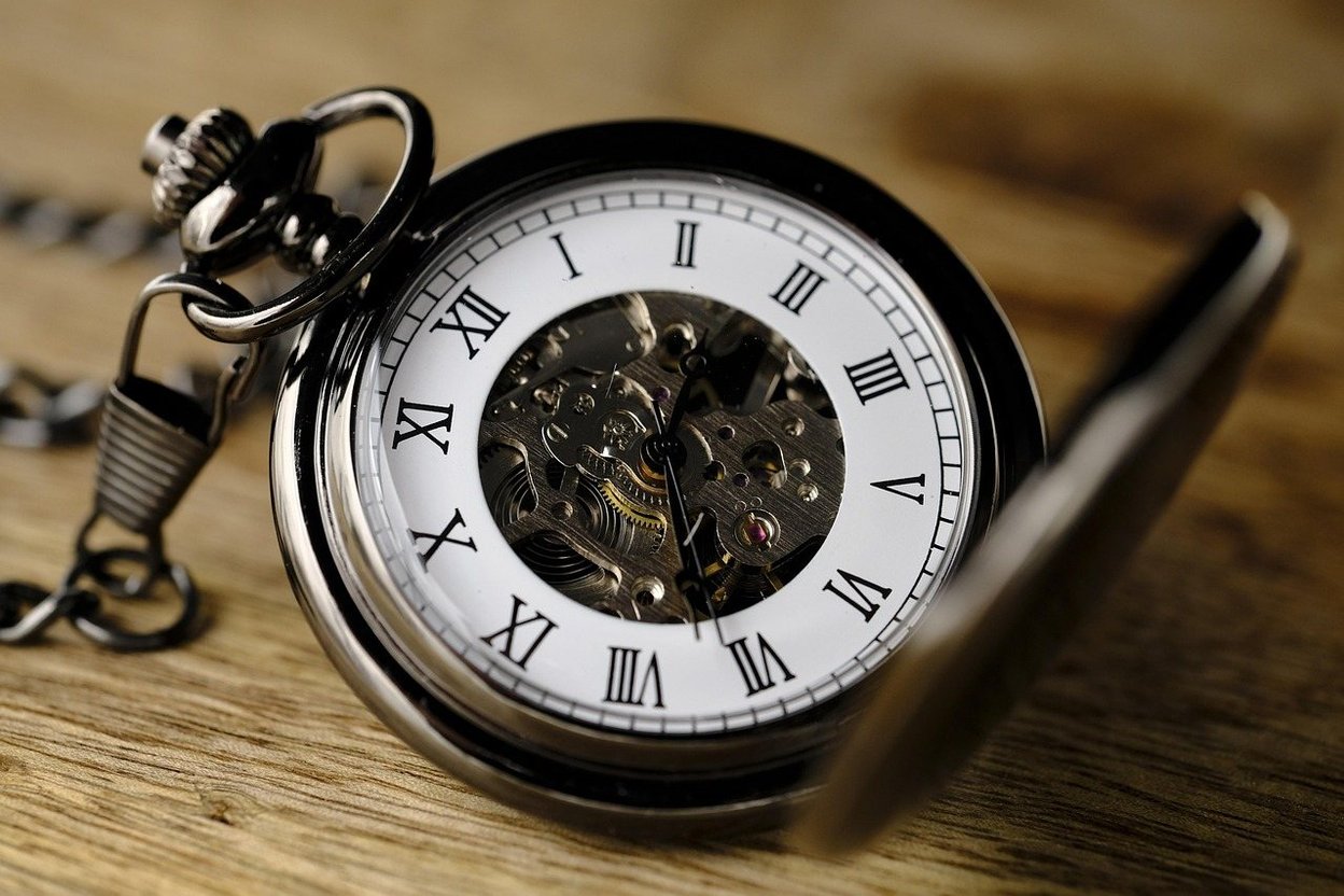 An open-faced silver pocket watch with Roman numerals on a wooden table.