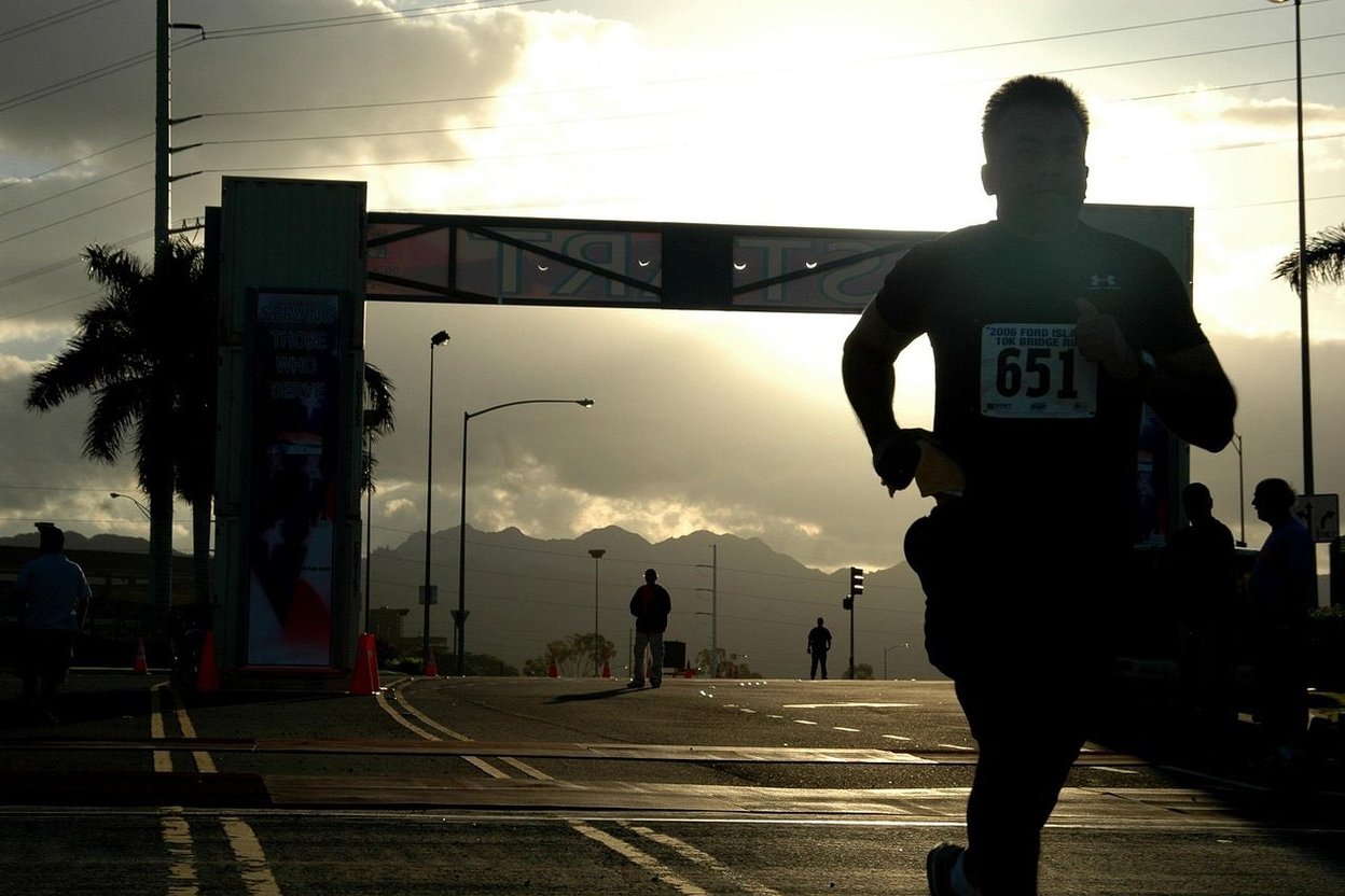 A marathon runner silhouetted against a sunset near a race arch, with mountains behind.