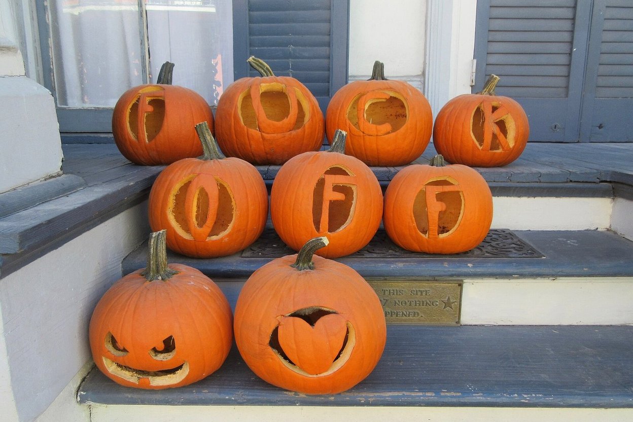 Carved jack-o'-lanterns on a front porch at dusk, with a wall calendar showing October 31 circled in the background.