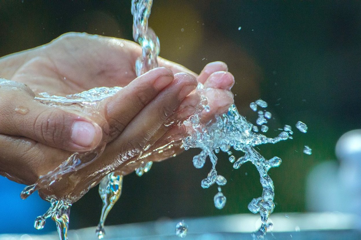 Hands washing under running water with splashes.